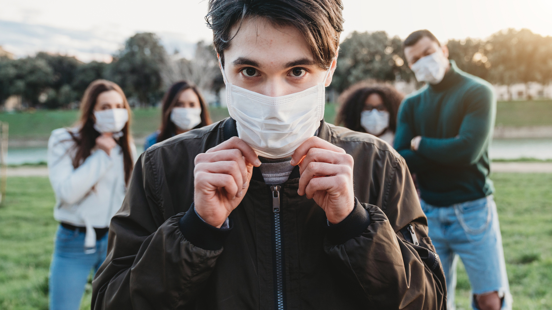 Young adult man wearing a pollution mask to protect himself from viruses. His friends are in the background.